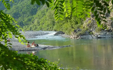 Un **lago vicino Milano con spiaggia** dove coppie si rilassano tra rocce e vegetazione lussureggiante.