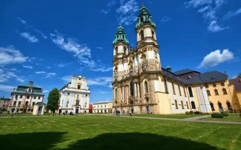 Barokowy kościół i klasztor na tle błękitnego nieba z chmurami. Piękne sanktuaria maryjne w Polsce zachwycają architekturą.
