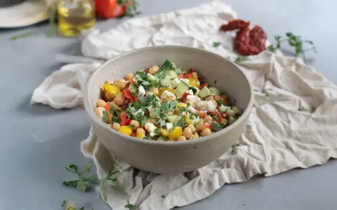 Ein bunter Kichererbsen Salat mit Gurken, Tomaten, Paprika und Feta, garniert mit frischer Petersilie.