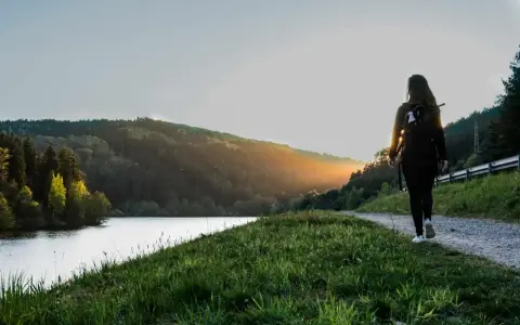 Frau mit Rucksack wandert auf einem Weg am See im Odenwald. Sonnenuntergang beleuchtet die Hügel.