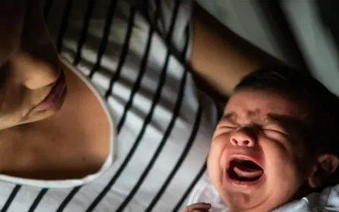 Ein schreiendes Baby, das von seiner Mutter getröstet wird. Vielleicht ein Zeichen für eine frühe Hochbegabung, die sich in intensiven Emotionen äußert.
