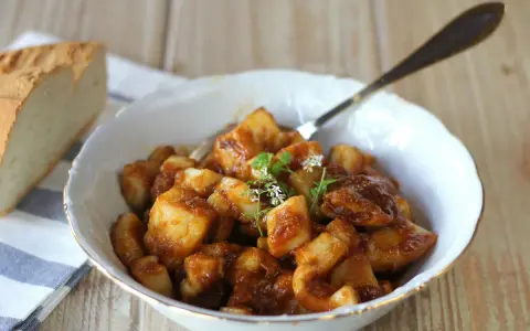 Un plato de sepia con patatas en salsa, decorado con hierbas frescas. Acompañado de pan rústico.