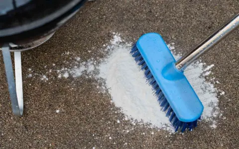 A blue brush is used to scrub a pile of white powder on a concrete patio, demonstrating how to clean concrete patio.