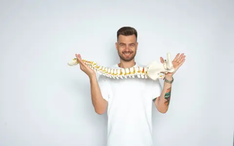 Uśmiechnięty mężczyzna trzyma model kręgosłupa, jakby prezentował jego elastyczność, niczym worek oponowy.