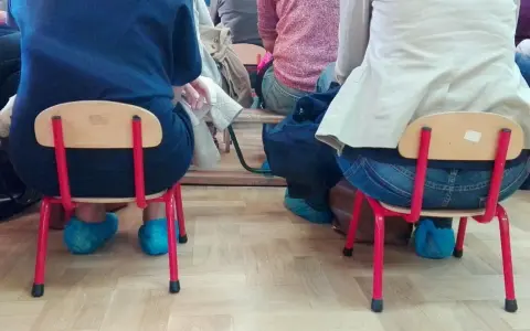 Dostateczny, jaka to ocena? Dzieci siedzą na małych krzesełkach w niebieskich ochraniaczach na buty.