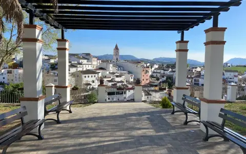 Un mirador con bancos y un arriate de flores ofrece vistas de un pueblo blanco con una torre de iglesia.