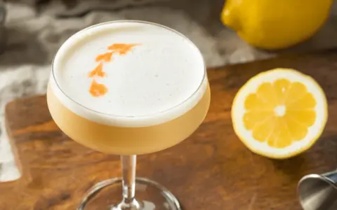 En läcker sifon drink med skummig topp, garnerad med orange mönster. Citroner och en jigger ligger bredvid.