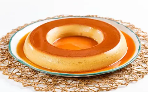 Un delicioso flan de café, con su caramelo dorado, reposa en un plato blanco con borde azul, sobre una esterilla tejida.