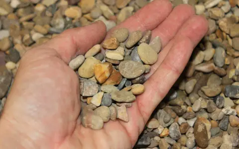 Mano sosteniendo una variedad de guijarros, mostrando que son los áridos, pequeños fragmentos de roca y minerales.