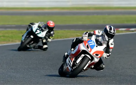 Dwóch motocyklistów w pełnym rynsztunku ściga się na torze. Jeden z nich, z numerem 11, pochyla się nisko w zakręcie, demonstrując emocje sportu motocyklowego.