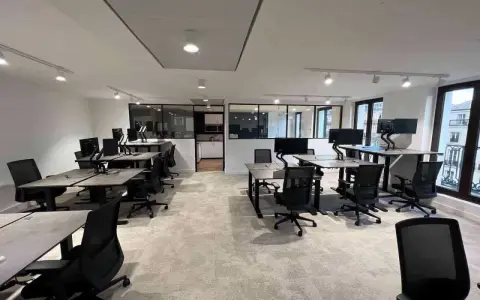 Bureau moderne avec postes de travail réglables en hauteur, écrans d'ordinateur et chaises ergonomiques. L'espace semble propre, mais on pourrait y sentir un air vicié sans fenêtres ouvertes.