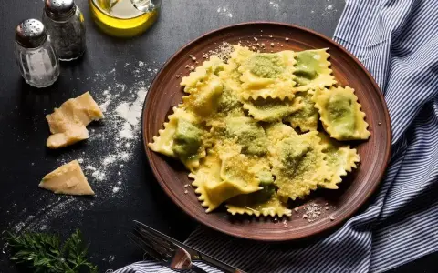 Pyszne ravioli z zielonym farszem, posypane parmezanem. Obok kawałki sera i przyprawy, gotowe do podania.