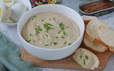 Una ciotola di cremosa salsa tonnata con maionese, guarnita con erba cipollina, accanto a pane tostato e uova sode.