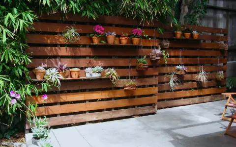 Pareti con bancali di legno ospitano piante grasse e fiori, creando un angolo verde.