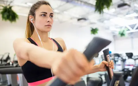 Junge Frau trainiert konzentriert auf einem Crosstrainer, um abzunehmen. Sie hört Musik über Kopfhörer.