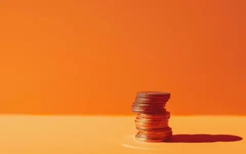 A stack of coins on an orange surface, symbolizing the business account requirements for financial growth.
