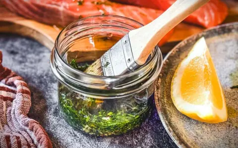 Marinade mit Kräutern und Zitrone bereit, um den Lachs zu verfeinern. Ein Pinsel liegt in der Glasflasche.