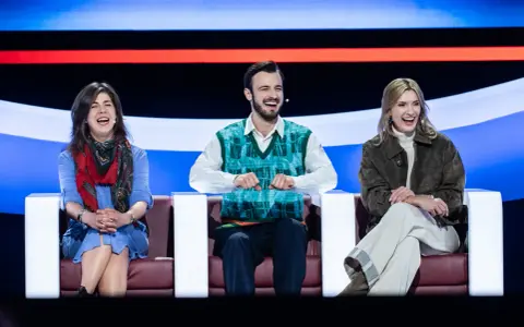 Trzy osoby śmieją się na kanapie, jakby oglądali koło fortuny kiedy w tv.