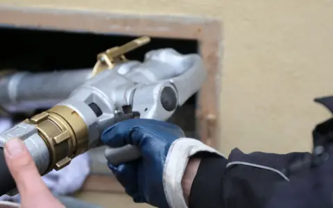 Main d'un technicien en gant bleu tenant un raccord de remplissage pour une vieille chaudière fioul.