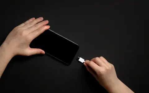 Dwie dłonie trzymają smartfon i biały kabel USB-C. Zastanawiasz się, do ilu procent ładować telefon, by zadbać o jego baterię?