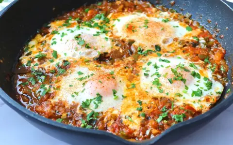 Huevos pochados en salsa de tomate y pimientos, un plato perfecto para tus recetas con huevos. Espolvoreado con perejil fresco.