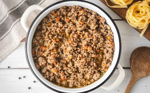 Un saporito ragù bianco in una pentola, pronto per condire la pasta. Pezzetti di carota e cipolla si mescolano alla carne macinata.