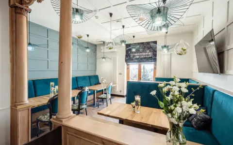 Wnętrze restauracji z turkusowymi kanapami, drewnianymi stołami i ozdobnymi lampami.