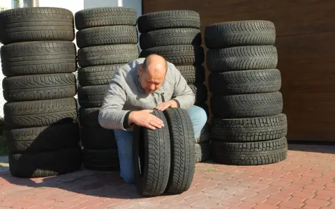 Mężczyzna sprawdza stan wyząbkowanych opon, które leżą obok stosów innych opon.