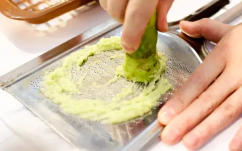 Świeże wasabi jest tarte na metalowej tarce, tworząc zieloną pastę. To właśnie tak powstaje prawdziwe wasabi.