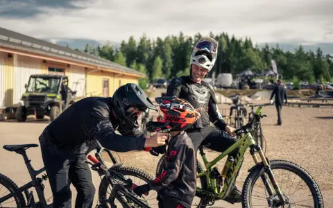 Två cyklister förbereder sig för mtb downhill. En vuxen hjälper ett barn med hjälmen.