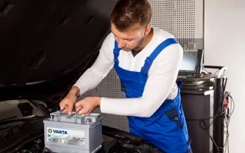 Mechanik w niebieskim kombinezonie wykonuje kodowanie akumulatora Varta w samochodzie.