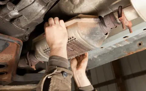 Mechanic inspecting a catalytic converter, a common culprit for why does my car smell like rotten eggs.