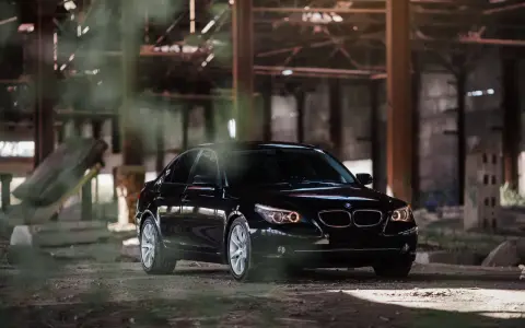 Czarny BMW 535d w opuszczonej hali, otoczony mgłą i gruzem.