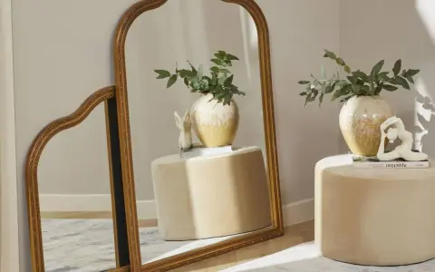 Dos espejos dorados, uno grande y otro pequeño, apoyados en la pared. Ideas para como colocar espejos pequeños en la pared.