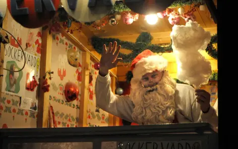 Tomten vinkar glatt och håller sockervadd. En påminnelse om vad betyder seder och julglädje.