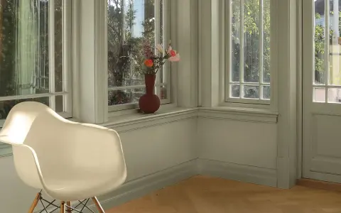 En ljus hall med en vit stol och en vas med blommor på fönsterbrädan. Väggarna är nymålade i en lugn grön nyans.
