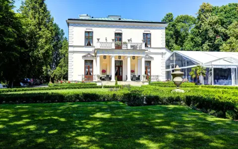Elegancki pałac Rozalin z kolumnowym portykiem i balkonem, otoczony zielonym ogrodem i nowoczesnym namiotem bankietowym.