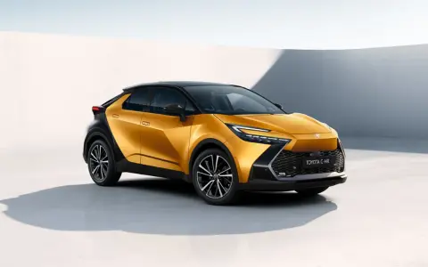 Nowy, złoty Toyota C-HR Hybrid z czarnym dachem prezentuje się dynamicznie na tle minimalistycznej architektury.