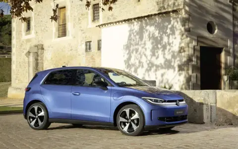 Niebieski samochód elektryczny VW ID. Polo stoi na brukowanej drodze przed kamiennym budynkiem.