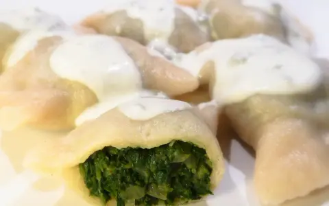 Pierogi ze szpinakiem polane sosem śmietanowym na białym talerzu.