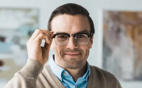 Mężczyzna w okularach dwuogniskowych poprawia je, uśmiechając się. Widać wyraźnie podział soczewek, jak wyglądają okulary dwuogniskowe.