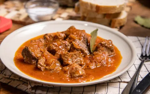 Sabrosa carne con tomate, guisada lentamente hasta quedar tierna, servida en un plato blanco con pan y sal al lado.