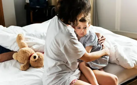 Mutter tröstet ihr Kind, das eine Panikattacke hat. Ein Teddybär liegt daneben.
