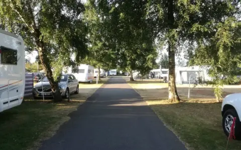 Väg leder genom rosendals camping, kantad av träd och husvagnar.