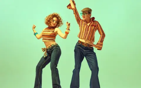 Para tańczy w rytm disco, ubrana w stylowe dzwony i wzorzyste topy, uosabiając modę lat 70.