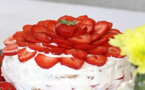 En vacker vegansk jordgubbstårta täckt med färska jordgubbar och fluffig grädde. Perfekt för sommaren!