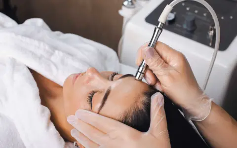 Aesthetician performs microdermabrasion on a woman's forehead. The question of microdermabrasion how often depends on skin type and goals.