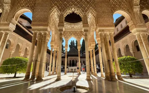 Intricate arches and columns of the Alhambra, a perfect postcard from Granada. Sunlight streams through, illuminating the detailed stonework.