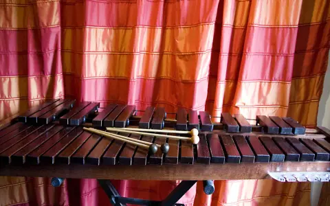 Ksylofon, instrument muzyczny na literę K, z pałeczkami, na tle czerwonej zasłony.