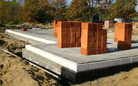 Budowa domu w toku. Stos pustaków i betonowa płyta fundamentowa. Zastanawiasz się, ile kosztują fundamenty?